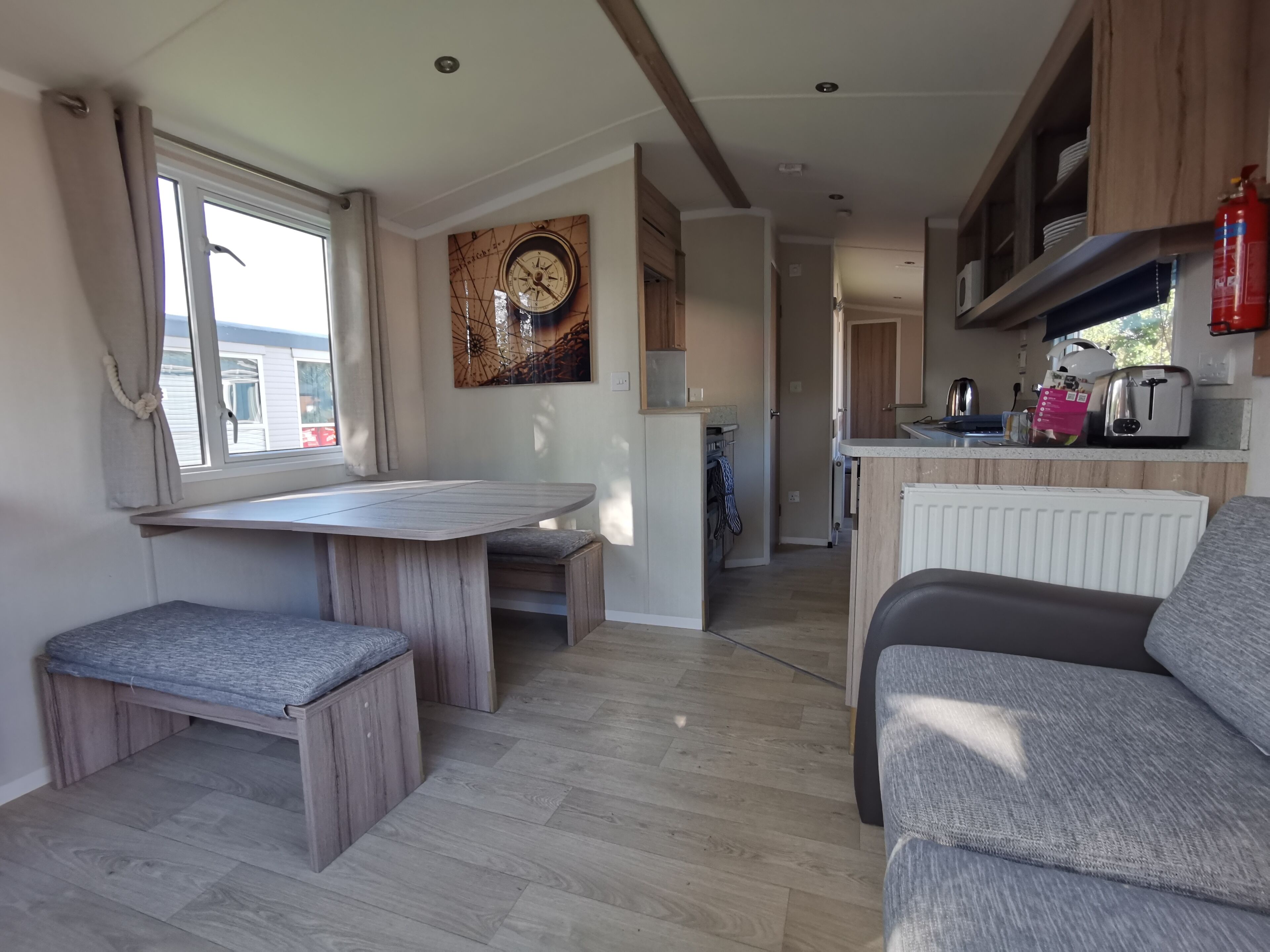 A modern kitchen with wooden cabinets, a dining area with a bench, and a grey sofa.