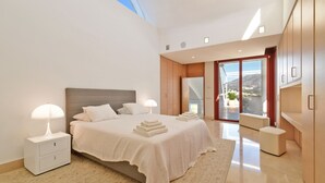 A modern bedroom with a large bed, bedside lamps, a view of the outdoors, and a sliding glass door leading to a balcony. - Extraordinary 7 BDRM Villa w Pool, Gym, Cinema (Marbella)