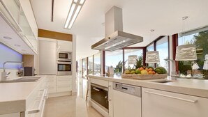 A modern kitchen with white cabinetry, stainless steel appliances, and a large window offering a view of the outdoors. - Extraordinary 7 BDRM Villa w Pool, Gym, Cinema (Marbella)