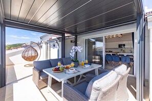 Un área de comedor exterior moderna con una mesa lista para el desayuno, mobiliario de mimbre y vistas del paisaje circundante.