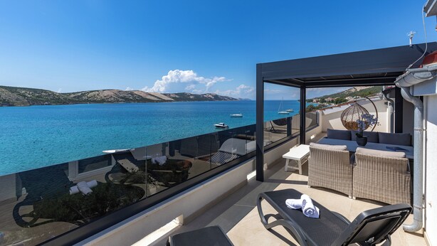 Un balcon offrant une vue dégagée sur la mer, des meubles en osier et une rambarde en verre.