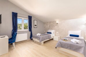 Habitación de hotel con dos camas, un escritorio, una silla, un radiador y una ventana con cortinas.