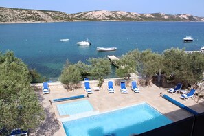 Zona de piscina con sillones de descanso y vista al mar con barcos.