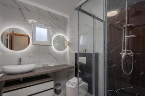 Un baño moderno con tocador de mármol, ducha con cerramiento de vidrio y un inodoro con toalla.
