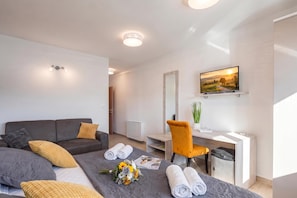 Ein modernes Hotelzimmer mit einem Bett, einem Schreibtisch, einem Stuhl, einem Fernseher und einer kleinen Pflanze.