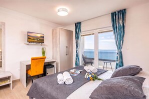 A hotel room with a bed, a desk, a chair, a television, and a view of the sea.