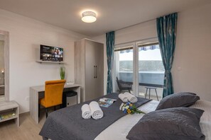 Une chambre d’hôtel avec un lit, un bureau, une chaise, une télévision et un balcon avec des rideaux.