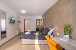 Een moderne slaapkamer met een bed, bureau, televisie en een plant.