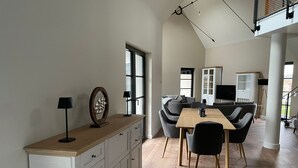 A modern living room with a dining area, featuring a wooden table, chairs, a sofa, and a TV. - Ferienhaus Inselglück in der Puddeminer Wiek (Poseritz)