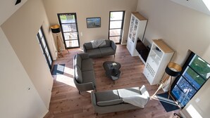 A spacious living area with a large L-shaped sofa, a coffee table, and a cabinet. There are two windows providing natural light and a view of the outdoors. - Ferienhaus Inselglück in der Puddeminer Wiek (Poseritz)