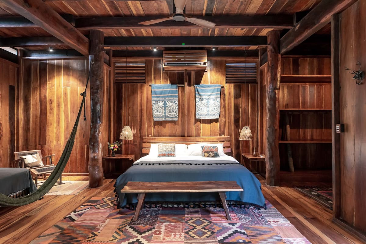 A rustic wooden room with a bed, a bench, and a hammock.