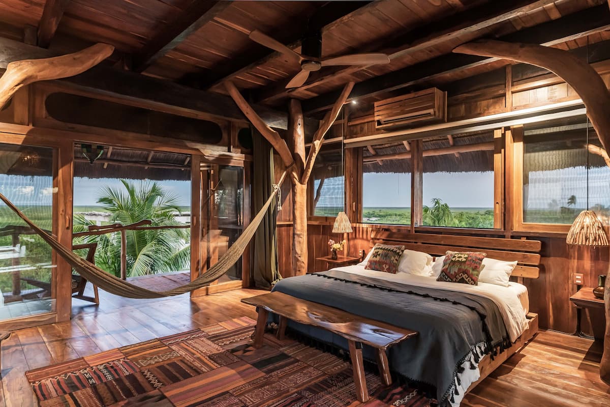 A wooden bedroom with a bed, bench, and hammock.