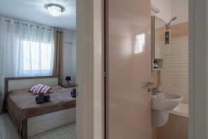 Une chambre à coucher avec un lit, une lampe de chevet et une fenêtre ornée de rideaux légers.