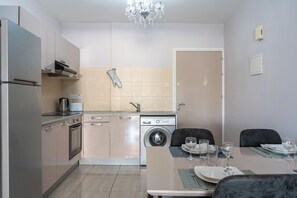 Une cuisine compacte équipée d’un lave-linge, d’une table à manger pour quatre personnes et d’un lustre.