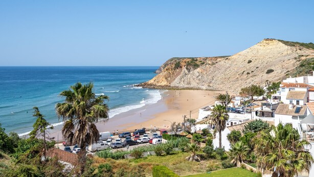 Une ville côtière avec une plage, des voitures garées et des bâtiments blancs aux toits rouges.