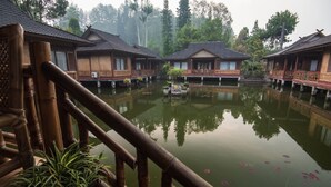 A traditional wooden building with a balcony, surrounded by a calm water body and greenery.
