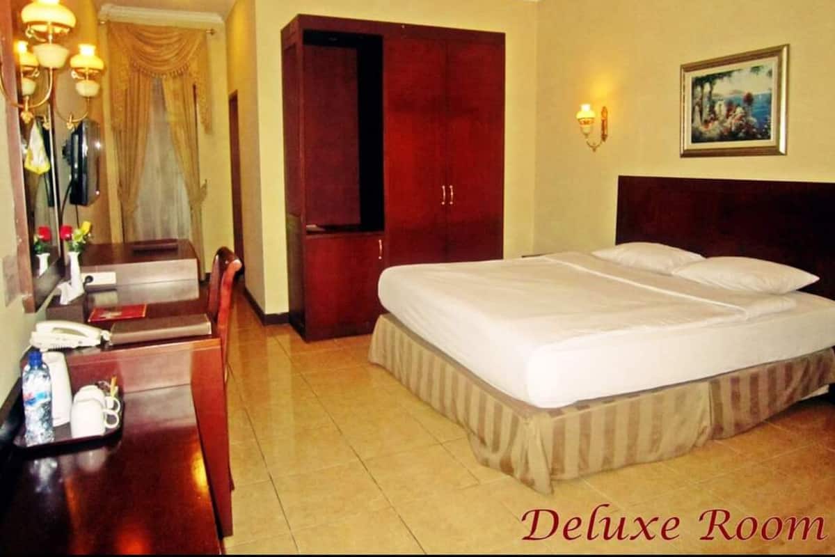 A deluxe room with a large bed, a desk with a telephone, and a painting on the wall.