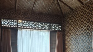 A room with two beds, a woven ceiling, and patterned walls.