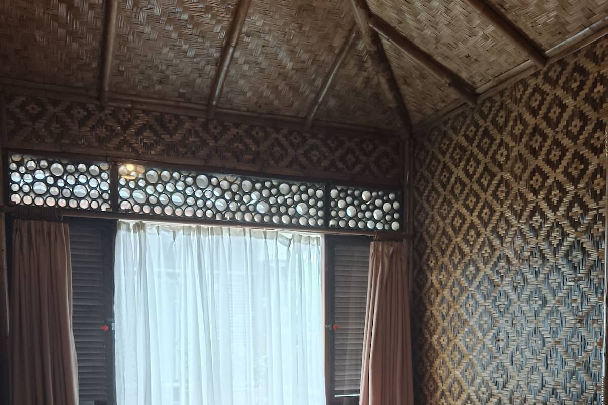 A room with two beds, a woven ceiling, and patterned walls.