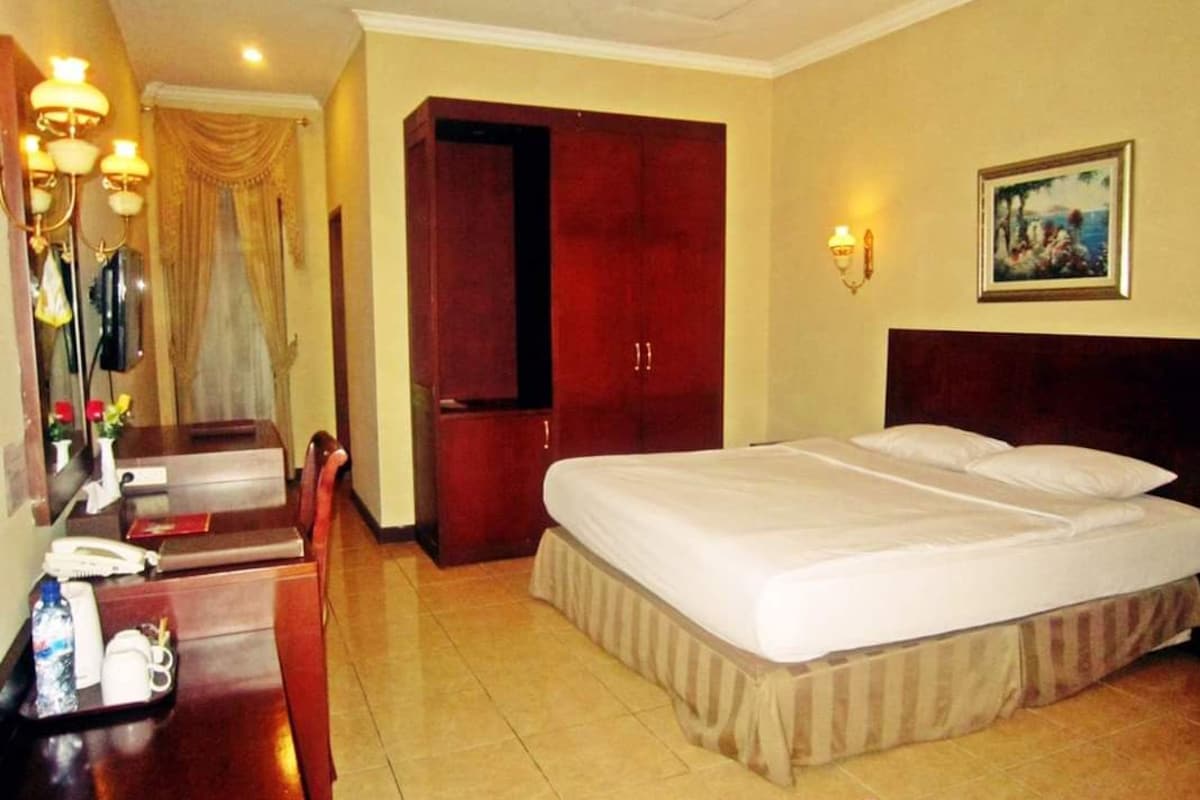 A deluxe room with a large bed, a desk with a telephone, and a painting on the wall.