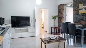 Een moderne woonkamer met een flatscreen-tv, een accentmuur van steen, een eethoek met stoelen en een klein bijzettafeltje.