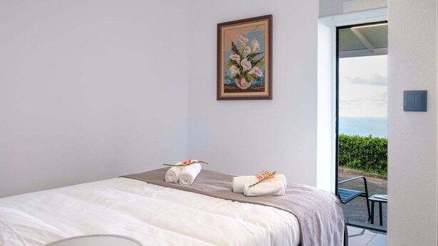 Een hotelkamer met een bed, een schilderij en uitzicht op zee.