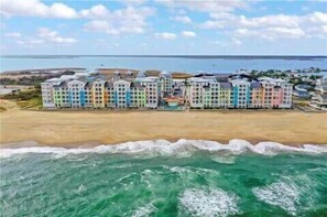 Un hotel frente a la playa con varios edificios coloridos, una playa de arena y el océano.