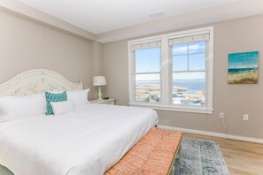 Un dormitorio con una cama grande, una mesita de noche, una lámpara, vista al mar y un cuadro en la pared.