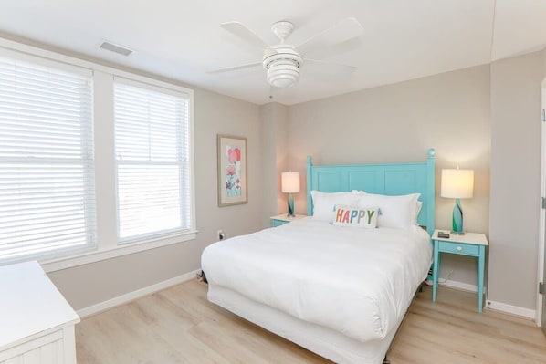 A bedroom with a large bed, two bedside tables with lamps, a ceiling fan, and a window with blinds.