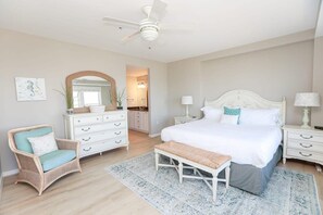 Un dormitorio con una cama grande, una silla, un banco, un aparador, un espejo y un ventilador de techo.
