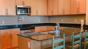 Una cocina con armarios de madera, un microondas de acero inoxidable, encimera de granito y una zona de bar con sillas.