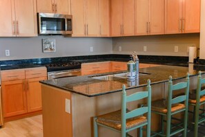 Una cocina con armarios de madera, un microondas de acero inoxidable, encimera de granito y una zona de bar con sillas.
