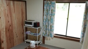 A room with a wooden table, a kettle, a shelf with items, and a window with curtains. - Cosmos Guesthouse Iya Valley (Miyoshi)