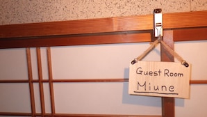 A wooden sign with the text "Guest Room Miune" hanging on a wall with a wooden panel design. - Cosmos Guesthouse Iya Valley (Miyoshi)