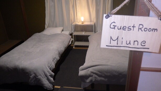 A guest room with two beds, a nightstand, and a sign indicating it is the guest room of Miune. - Cosmos Guesthouse Iya Valley (Miyoshi)