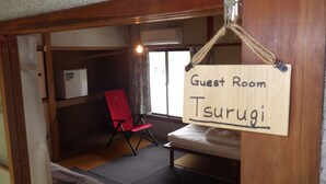 A small, compact room with a single bed, a red chair, and a sign indicating it is a guest room named Tsurugi. - Cosmos Guesthouse Iya Valley (Miyoshi)