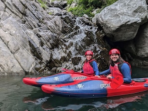 Two people in red helmets and life jackets on a red and blue raft.