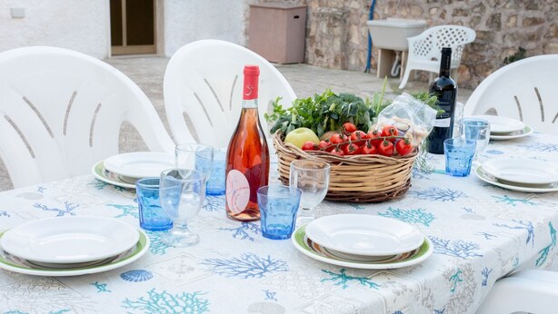 A table set for a meal with plates, glasses, a bottle, and a basket of fresh vegetables.