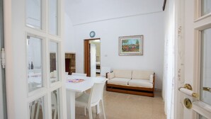 A room with a white table, white chairs, a beige sofa, and a painting on the wall.