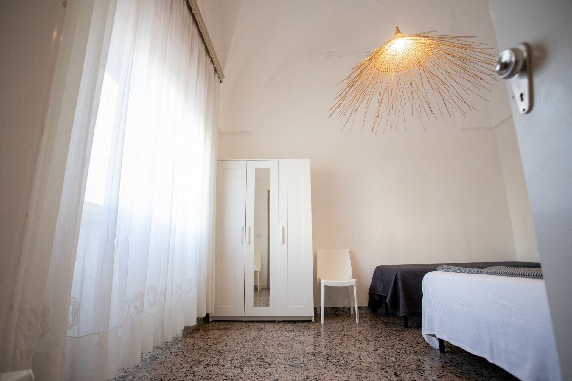 A hotel room with a bed, a chair, a wardrobe, and a unique ceiling light fixture.