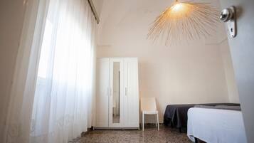 A hotel room with a bed, a chair, a wardrobe, and a unique ceiling light fixture.