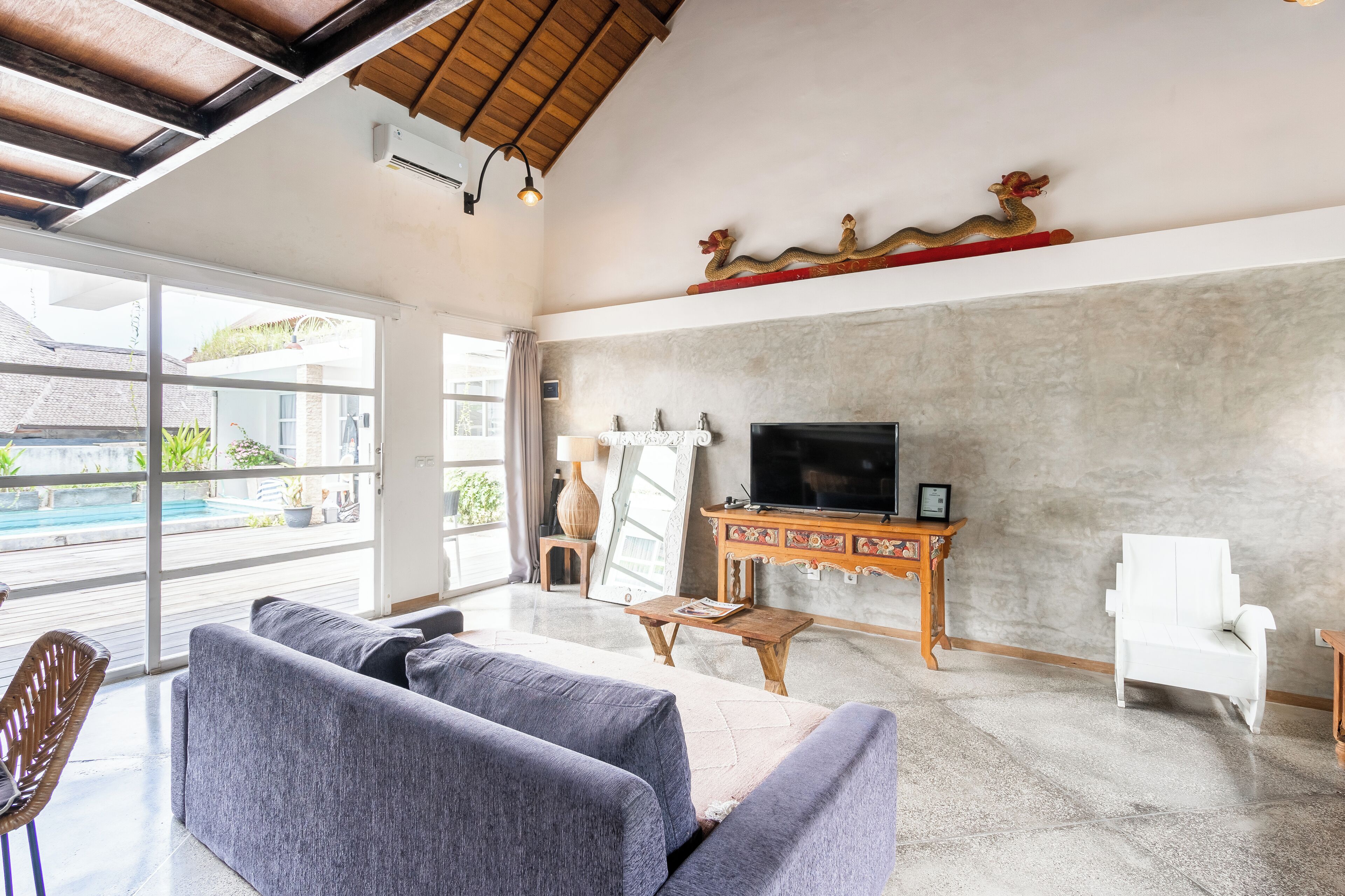 A spacious living area with a large window, a flat-screen TV, a white chair, and a wooden coffee table.