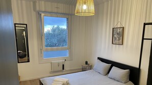 Ein Schlafzimmer mit einem großen Bett, einem Fenster mit Blick auf Bäume, einem Heizkörper und einem kleinen Tisch mit einer Lampe.