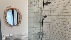 Ein Badezimmer mit einer gläsernen Duschkabine, einem runden Spiegel mit Holzrahmen und einem Waschbecken mit Natursteinbecken.