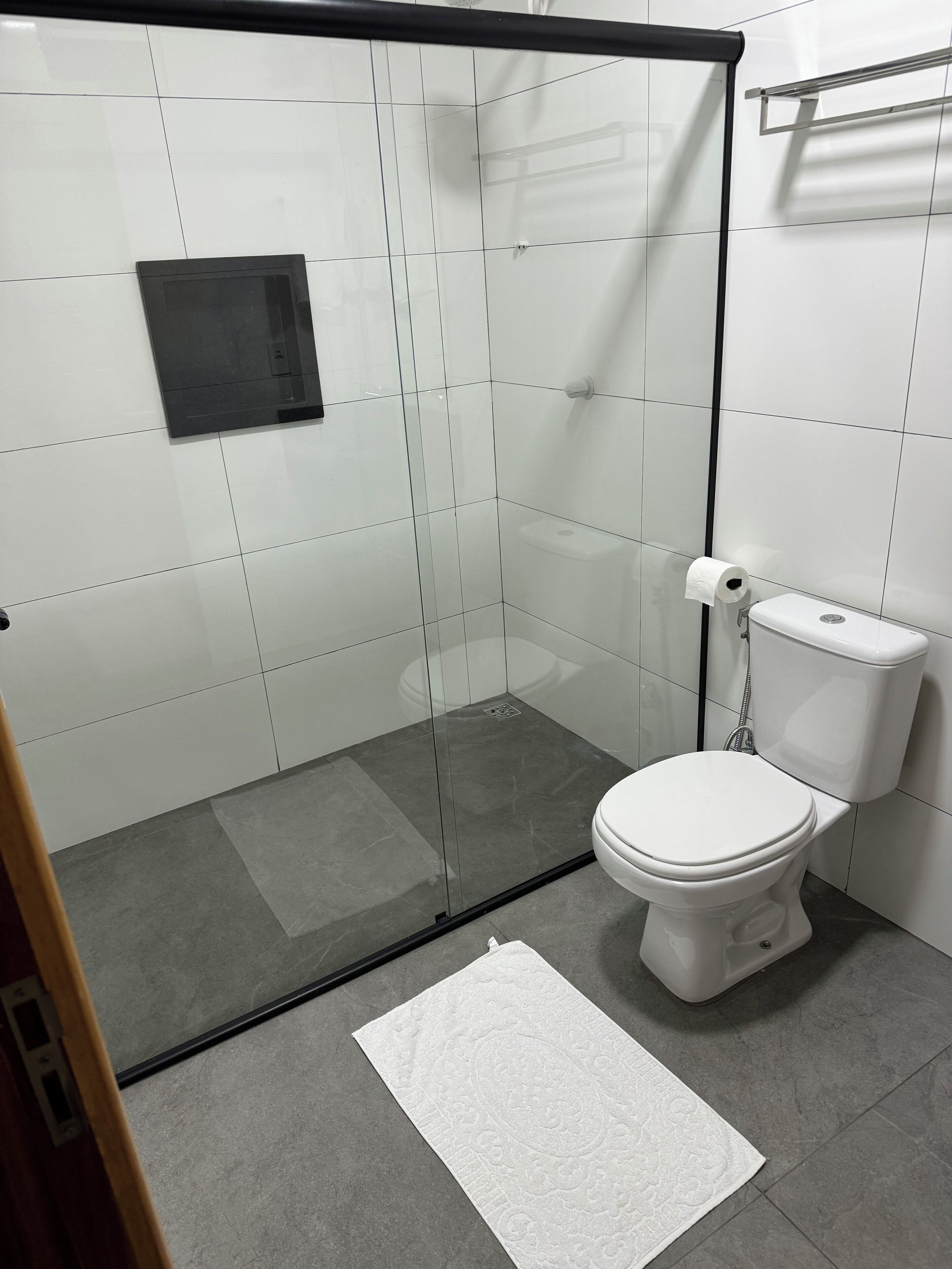 Un baño moderno con ducha de vidrio, inodoro blanco y un lavamanos pequeño.