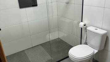 Un baño moderno con ducha de vidrio, inodoro blanco y un lavamanos pequeño.