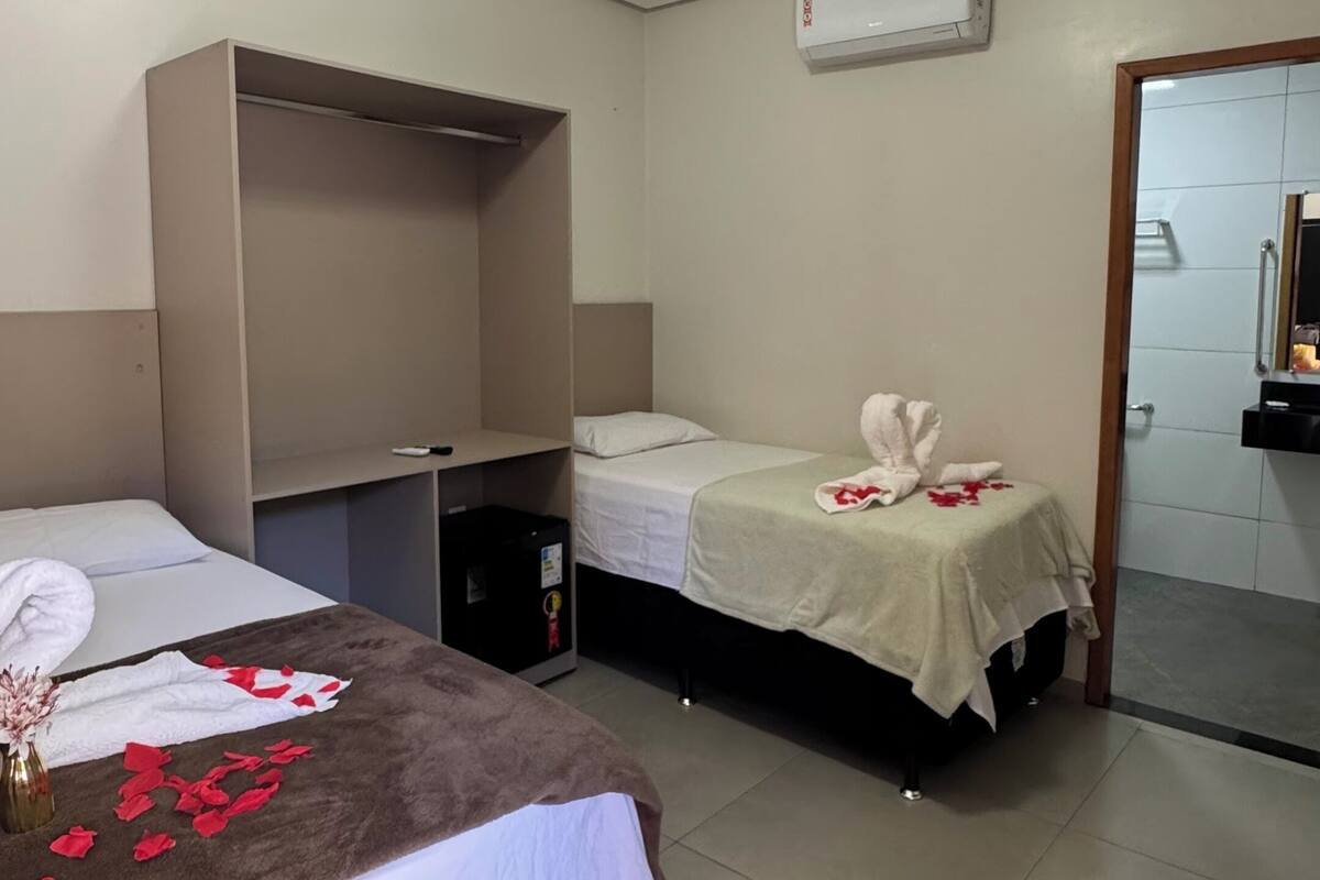 A hotel room with two beds, a wardrobe, a mirror, and an air conditioning unit.