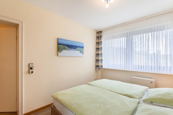 Une chambre à coucher avec un lit, un tableau, une fenêtre avec des rideaux et un thermostat.
