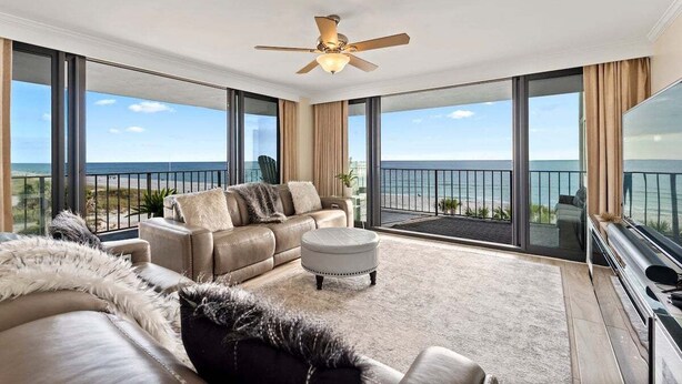 A spacious balcony with a view of the ocean, a ceiling fan, and a large flat-screen TV.