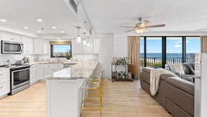 A modern kitchen with a central island, bar stools, and a view of the ocean.
